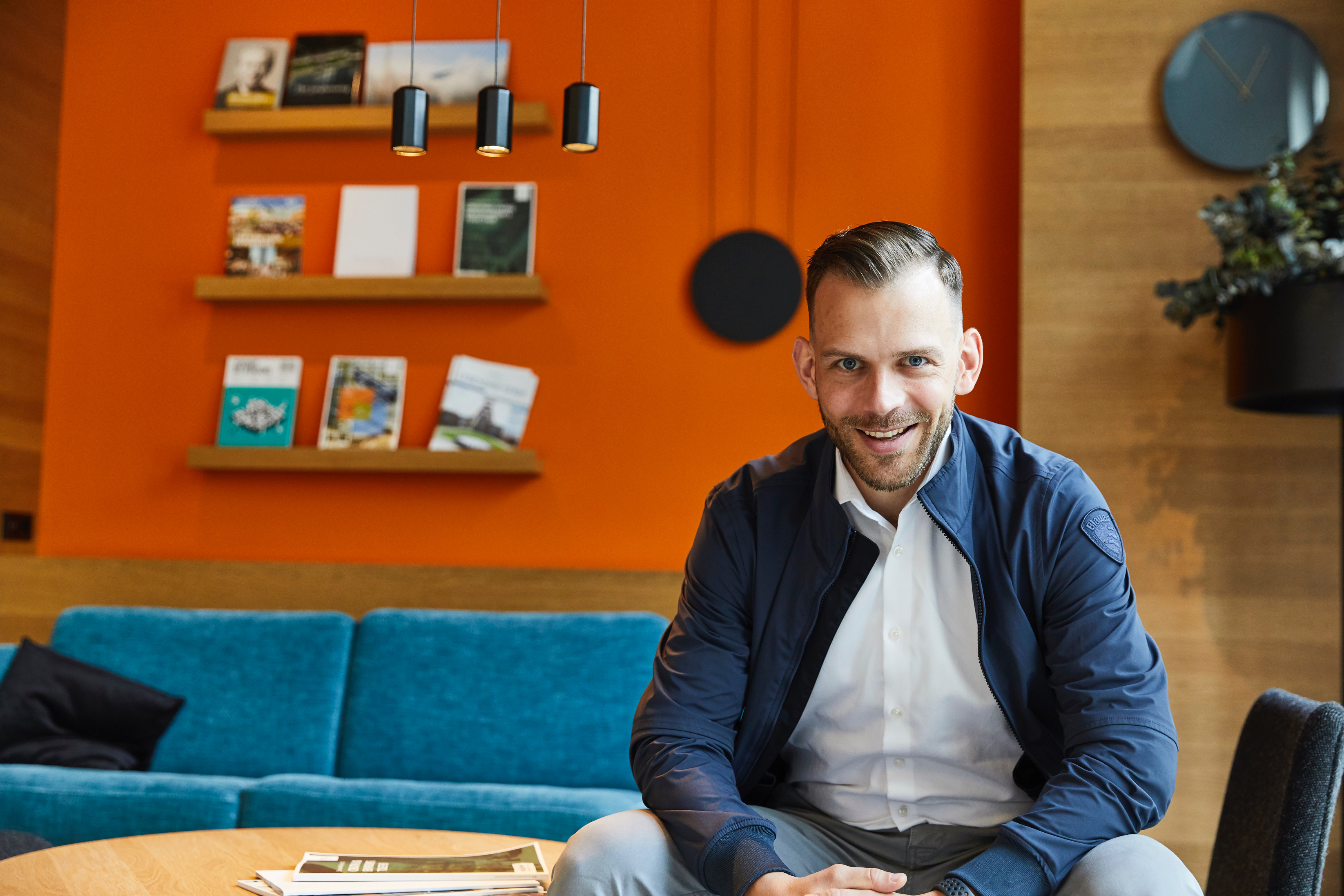 Dr. Christian Schlicht sitzend vor einer orangefarbenen Wand mit Bücherregal