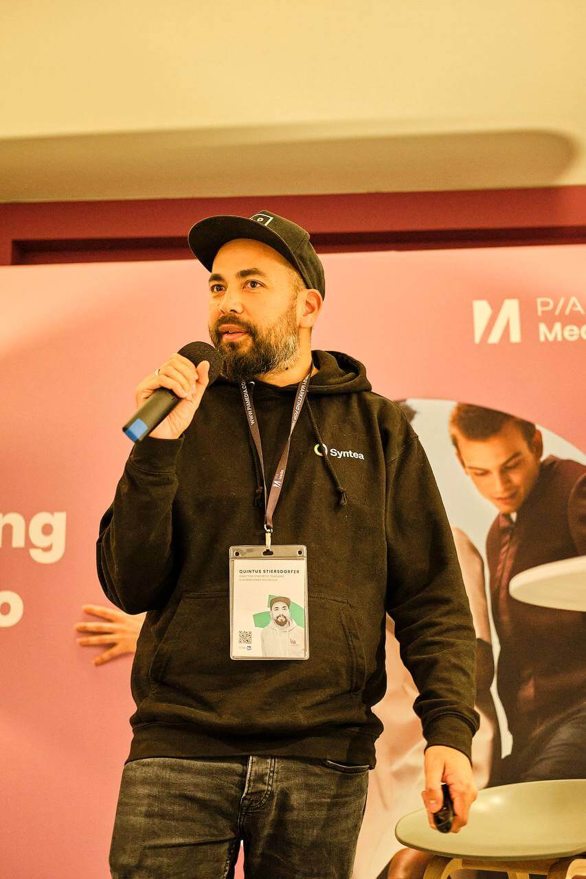 Quintus Stierstorfer spricht im Syntea-Hoodie vor einer Konferenz-Stellwand