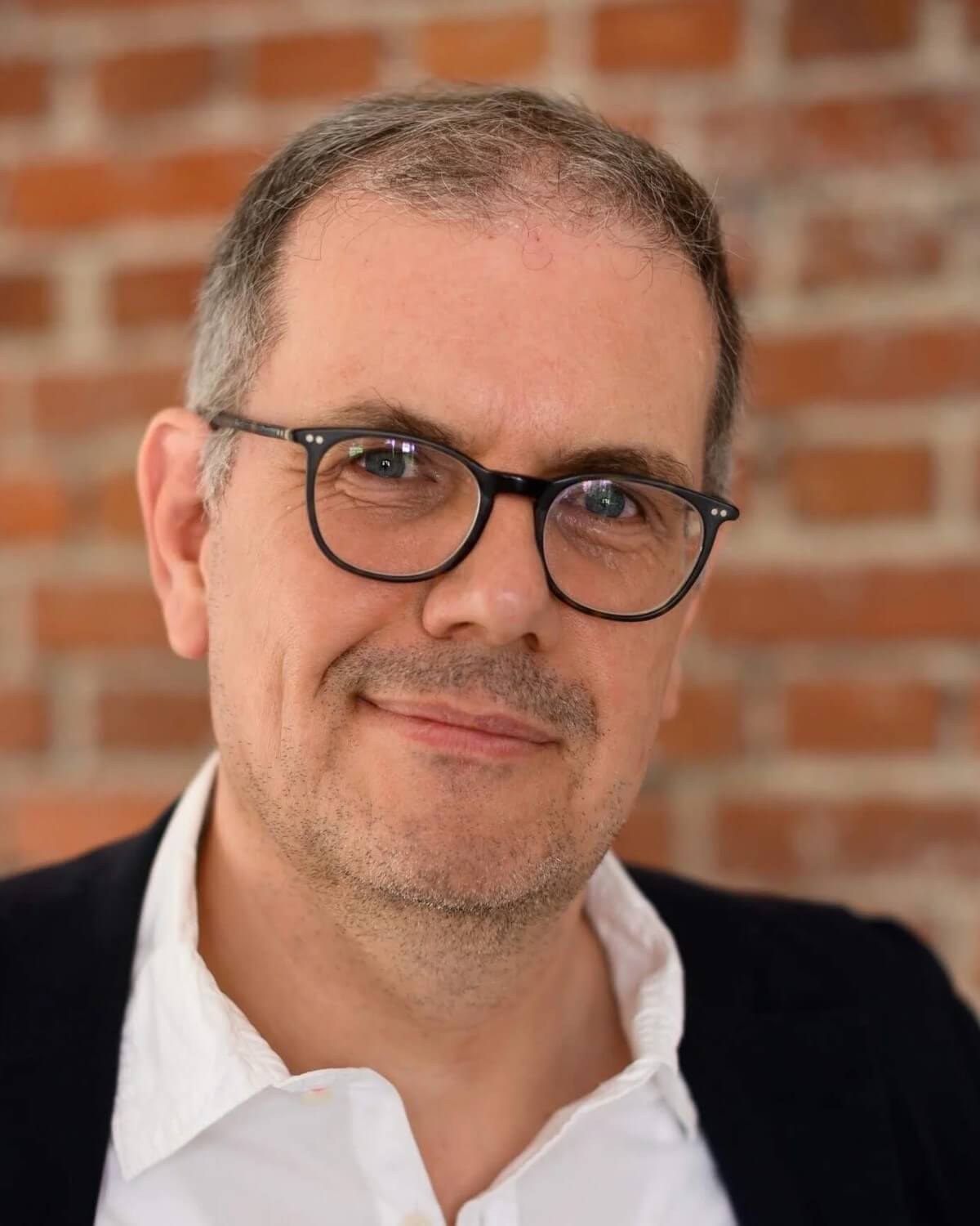 Björn Ognibeni im weißen Hemd vor einer roten Backsteinwand