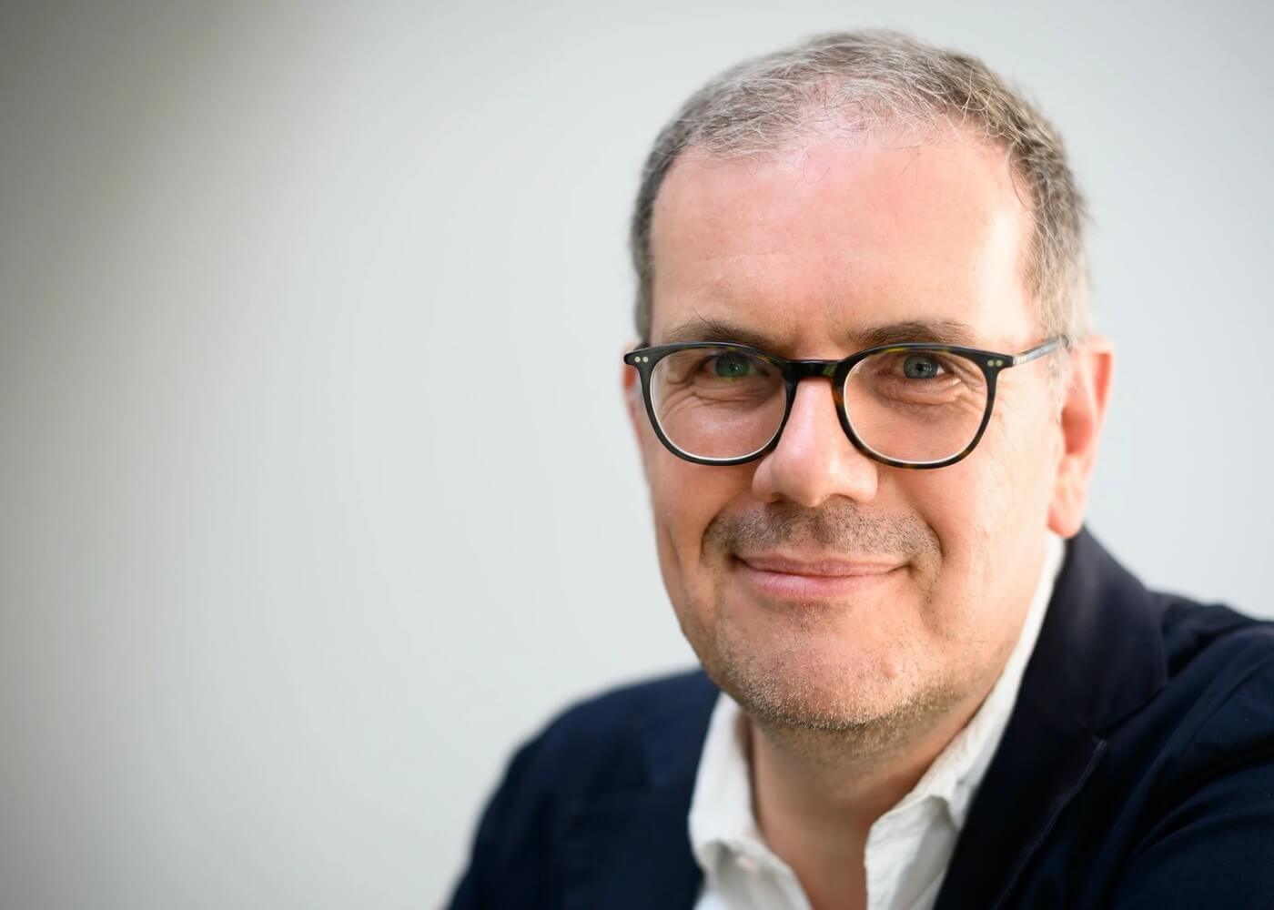 Björn Ognibeni vor hellem Studiohintergrund, Blick in die Kamera