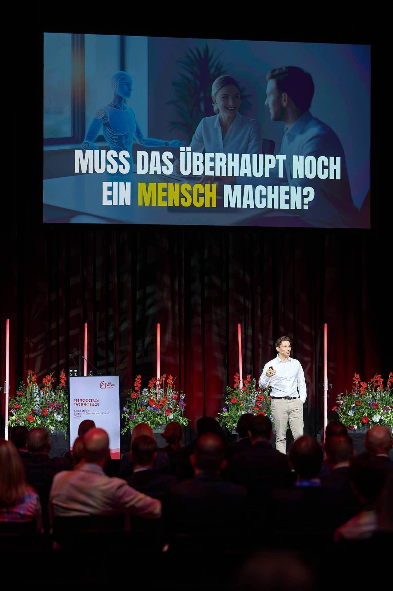 Dr. Hubertus Porschen auf einer Bühne vor Publikum, auf der Leinwand die Frage Muss das überhaupt noch ein Mensch machen