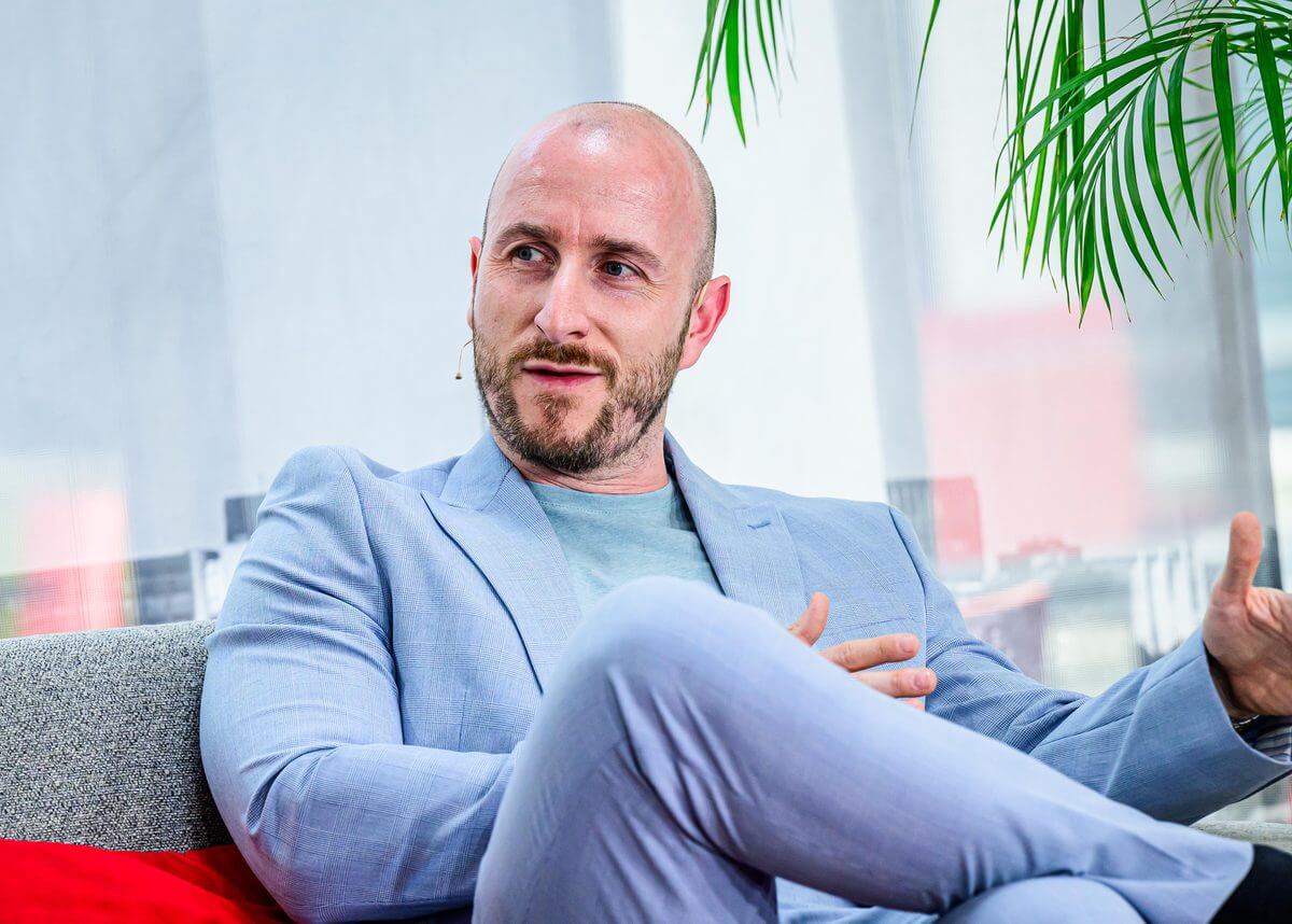 Florian Jörgens im hellblauen Sakko im Gespräch auf einem Sofa