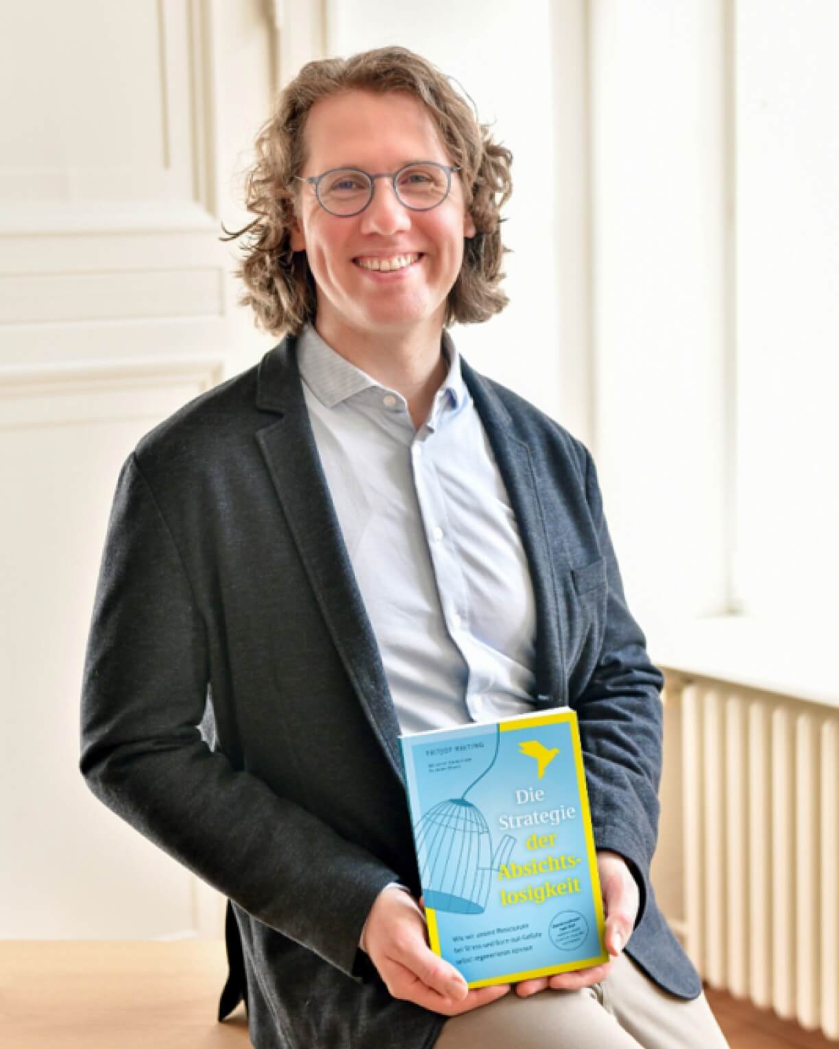 Fritjof Nelting – Keynote Speaker für Gesundheit in Unternehmen Fritjof Nelting im dunklen Sakko mit seinem Buch „Die Strategie der Absichtslosigkeit“ in der Hand